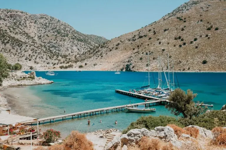 Voiliers amarrés à une jetée en bois dans une baie turquoise entourée de collines rocheuses