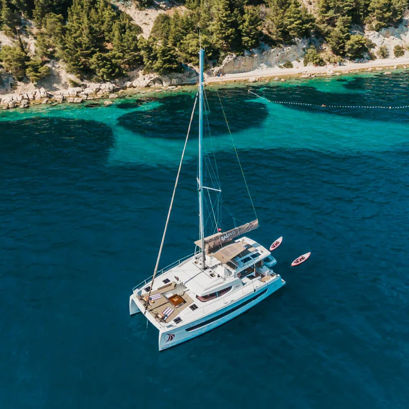 Aerial view of a Bali 4.6 catamaran anchored beside a rocky, wooded coast