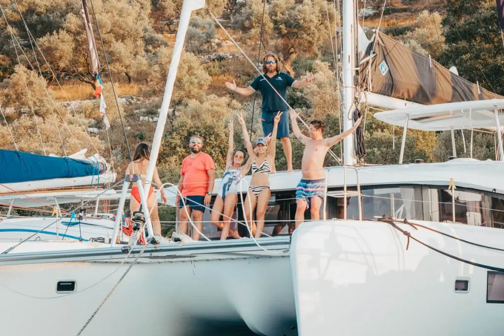 Un grup de oameni stând pe puntea unui catamaran ancorat lângă o coastă împădurită