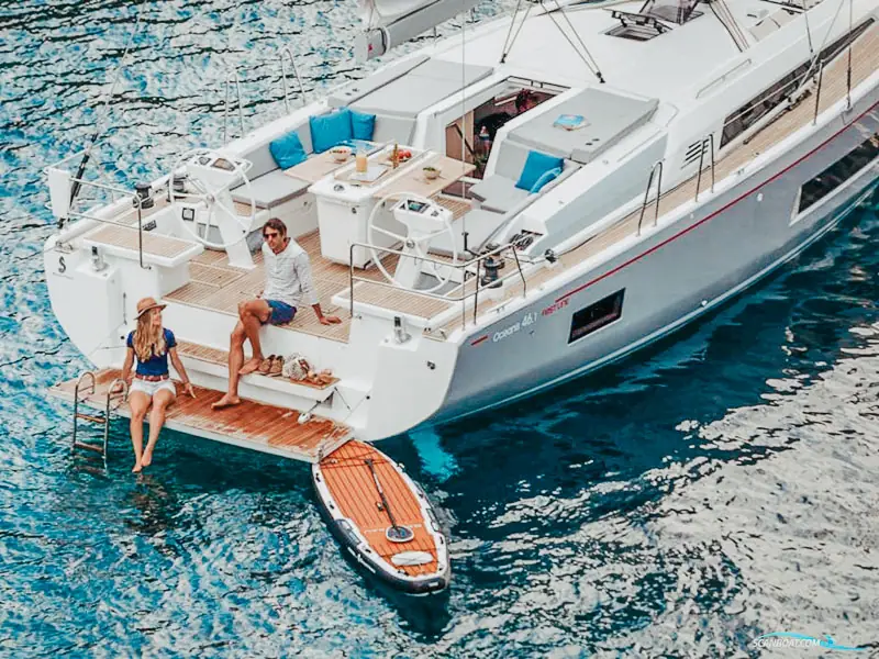 Two people relaxing on a sailing yacht's stern platform with a paddleboard alongside